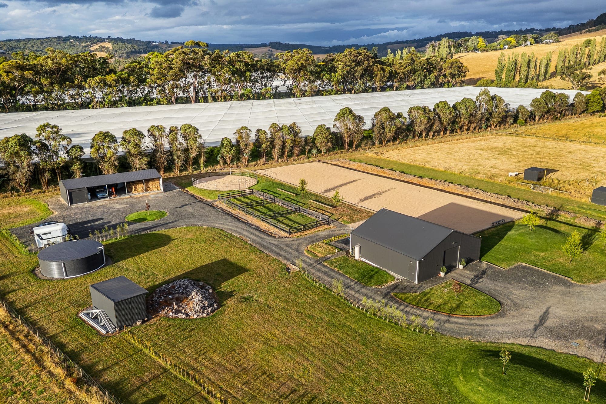 Elevated view of an equestrian acreage in late light, arena, round yard, sheds and paddocks with hills behind