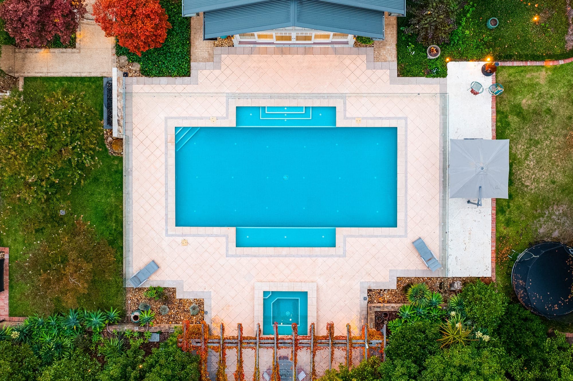 Directly overhead view of a formal rectangular pool at dusk, symmetrical paving framed by autumn trees