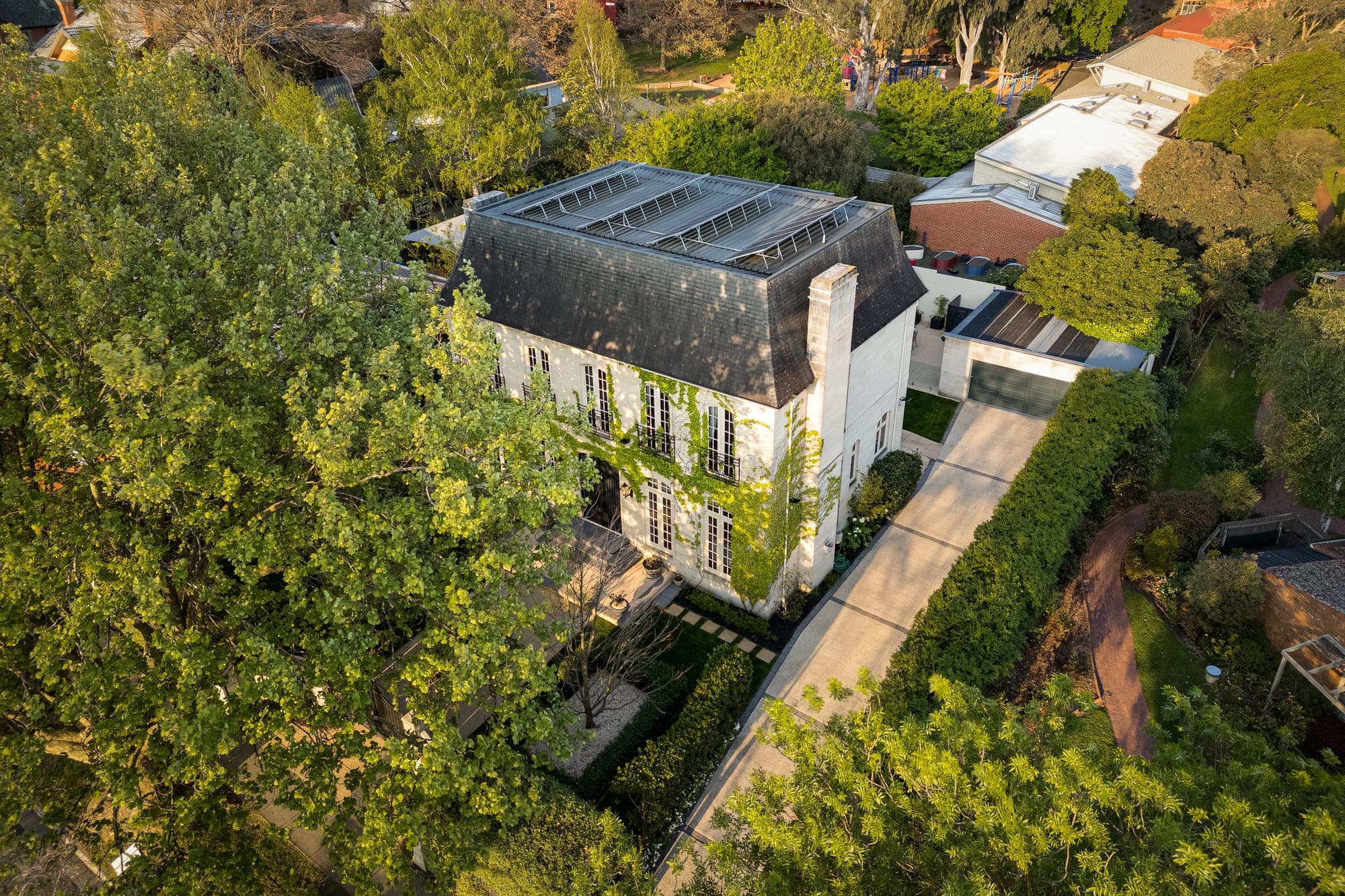 Raised aerial of a French provincial home with a mansard roof and ivy across its facade, set in an established garden