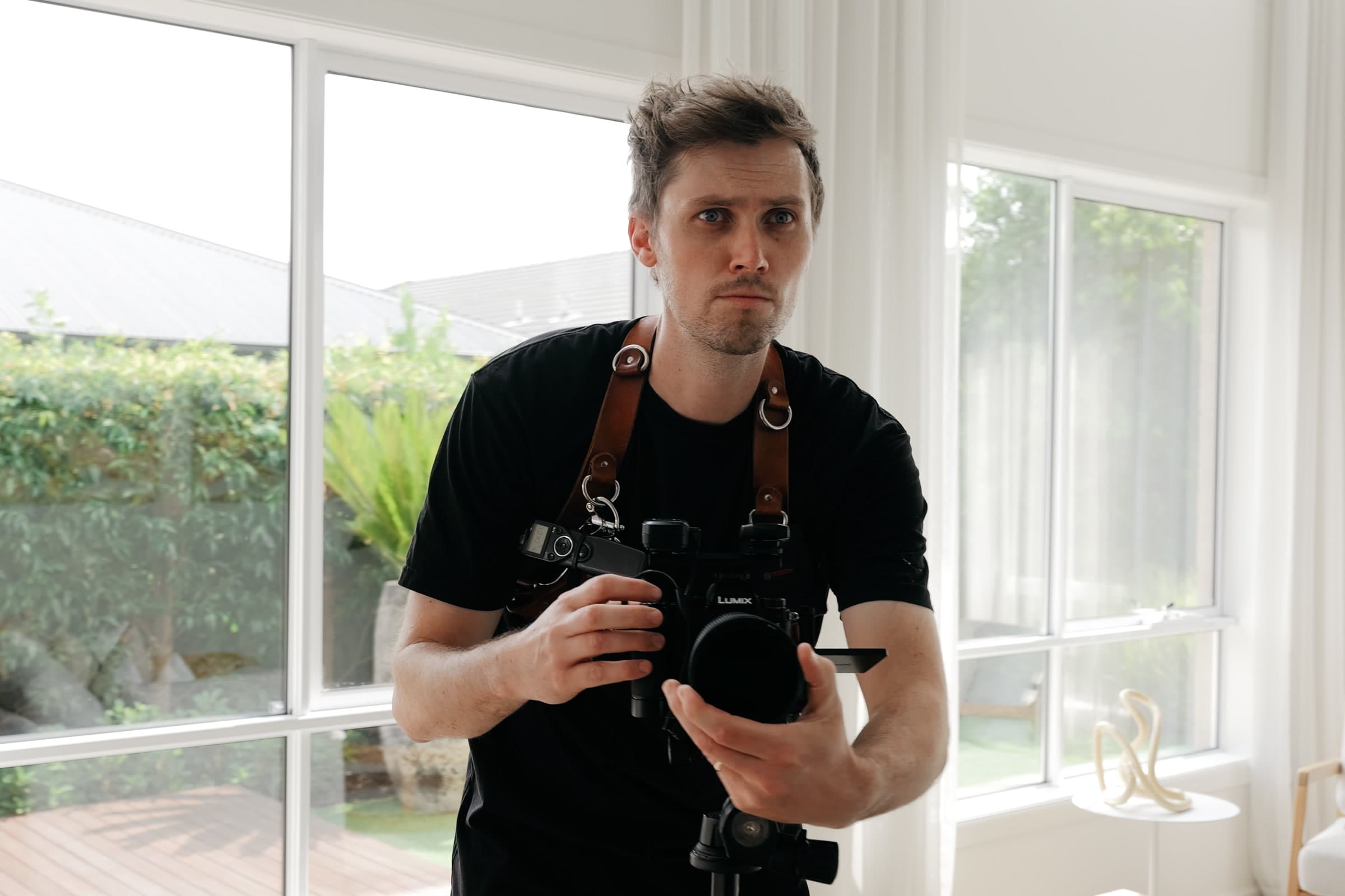 Justin on location, framing a shot on a tripod-mounted camera in a bright living room