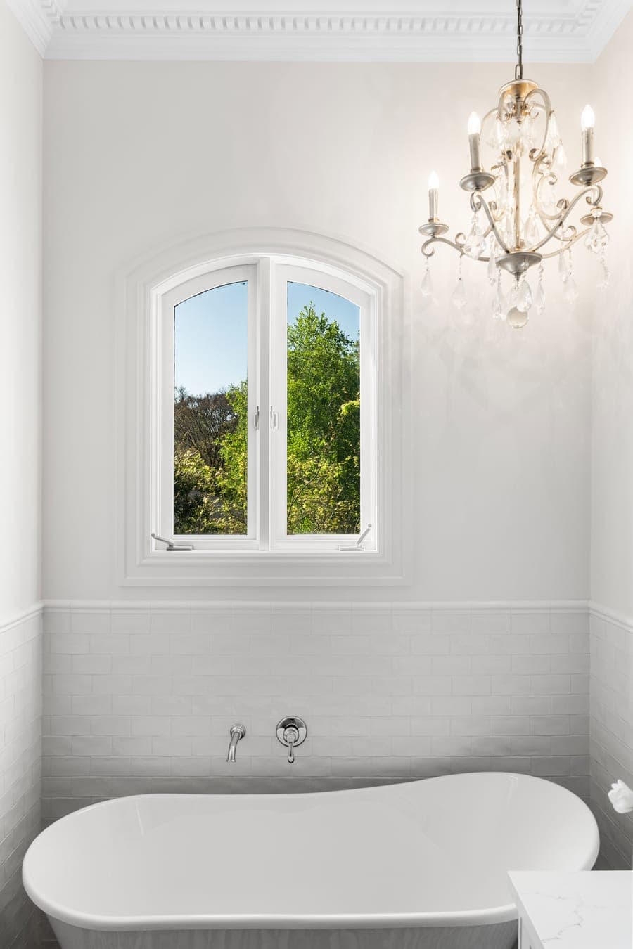 Bathroom with a freestanding oval tub beneath an arched window and a crystal chandelier above