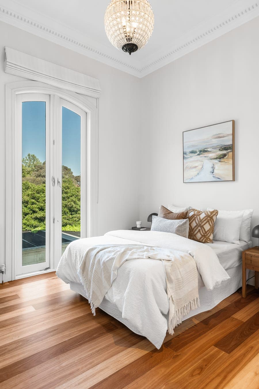 Bedroom in white linen with framed artwork and french doors opening to the garden