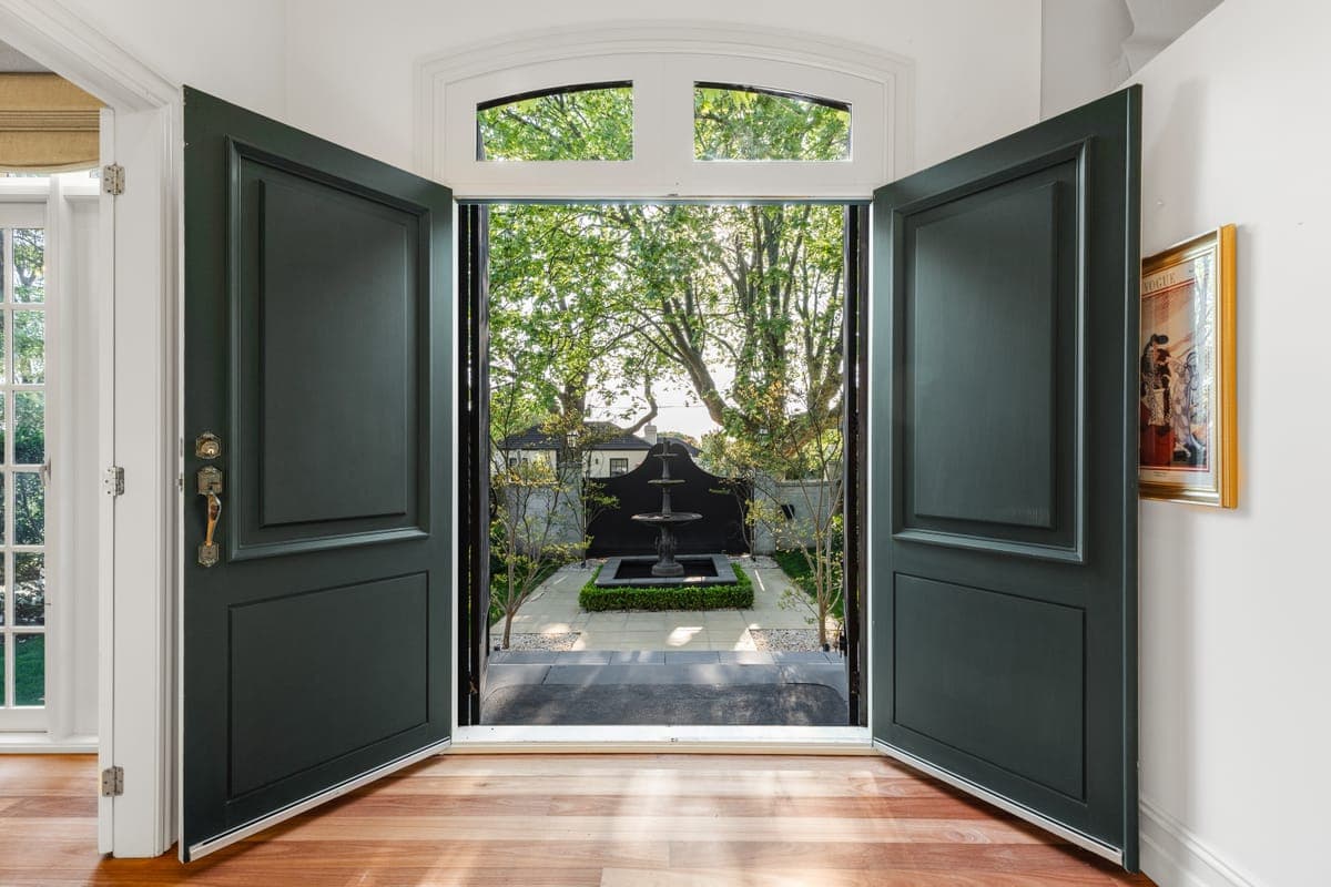 Tall deep green double doors standing open onto a clipped courtyard garden