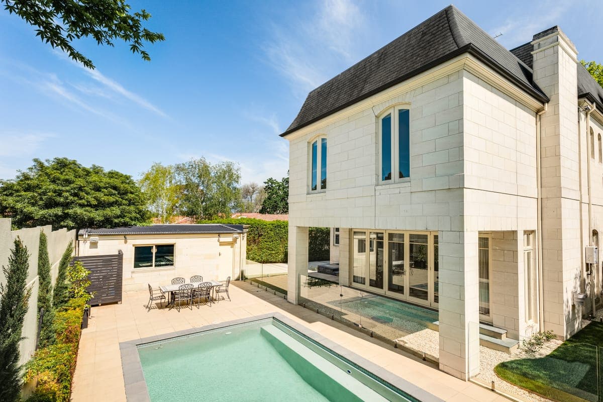 The rear of the house across a lap pool, alfresco under the upper storey and clipped hedging along the boundary