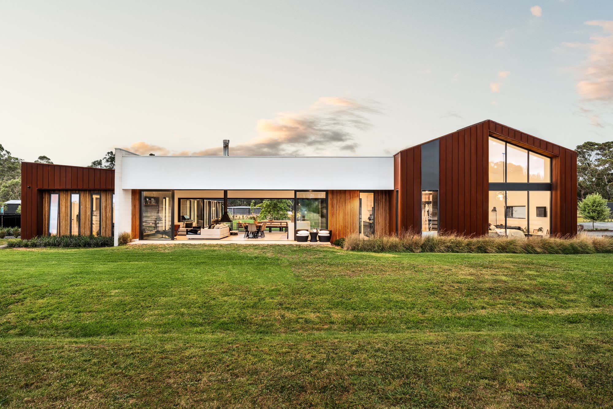 Long low facade of a rural home at dusk, lit from within
